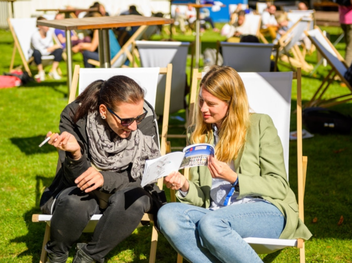 Frauen sitzen in der Sonne auf Stühlen draußen und schauen gemeinsam auf das Programm